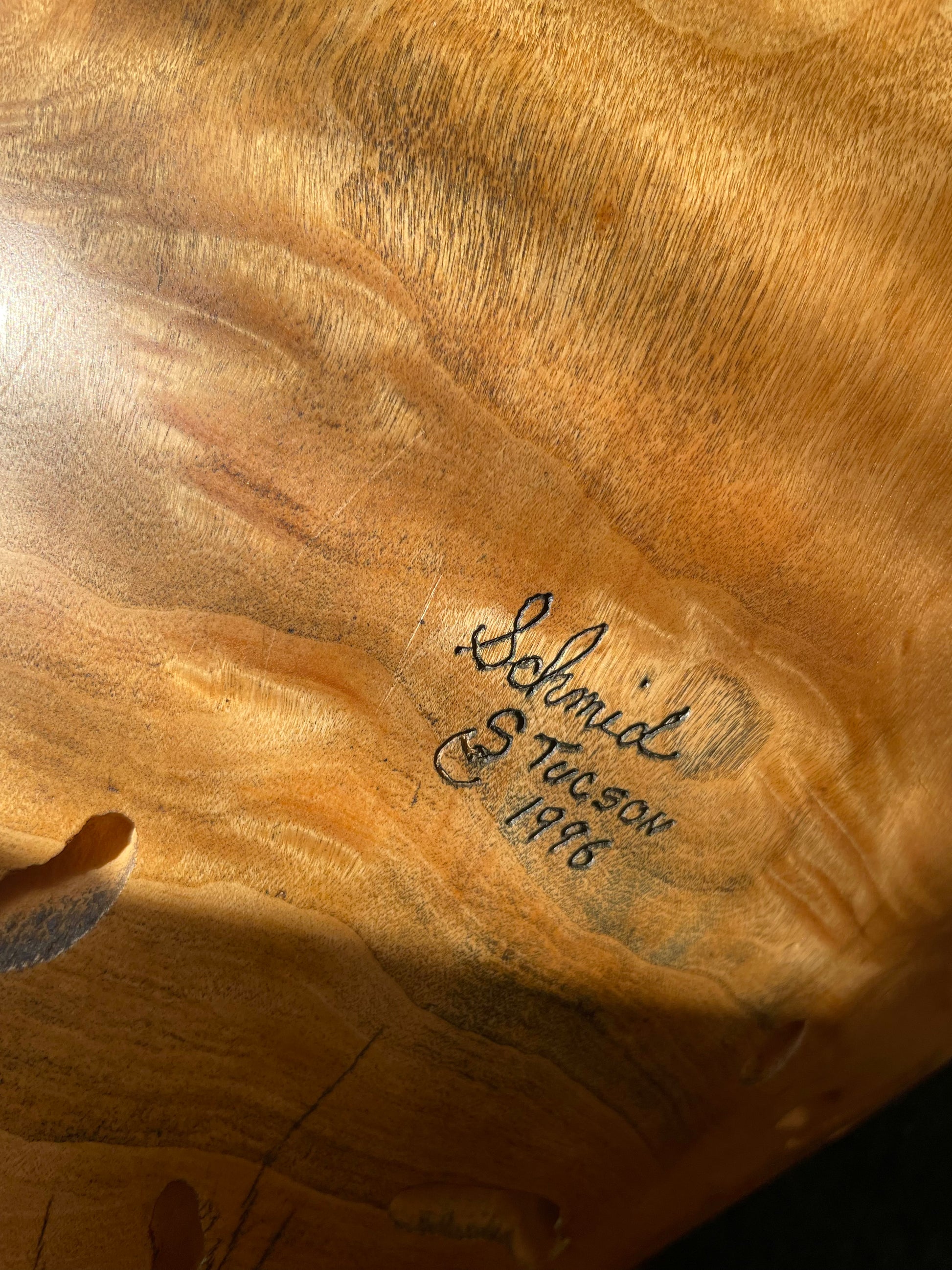 Close-up of a polished wood surface with natural grain and a handwritten signature reading ’Schmid, S. Tucson 1996'.