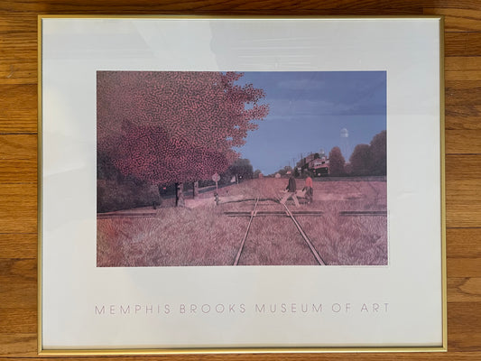 Framed art print from the Memphis Brooks Museum of Art, featuring a stylized railroad scene with a large pinkish-brown tree, two figures walking across the tracks, and a blue sky, mounted in a gold frame on a wood surface.