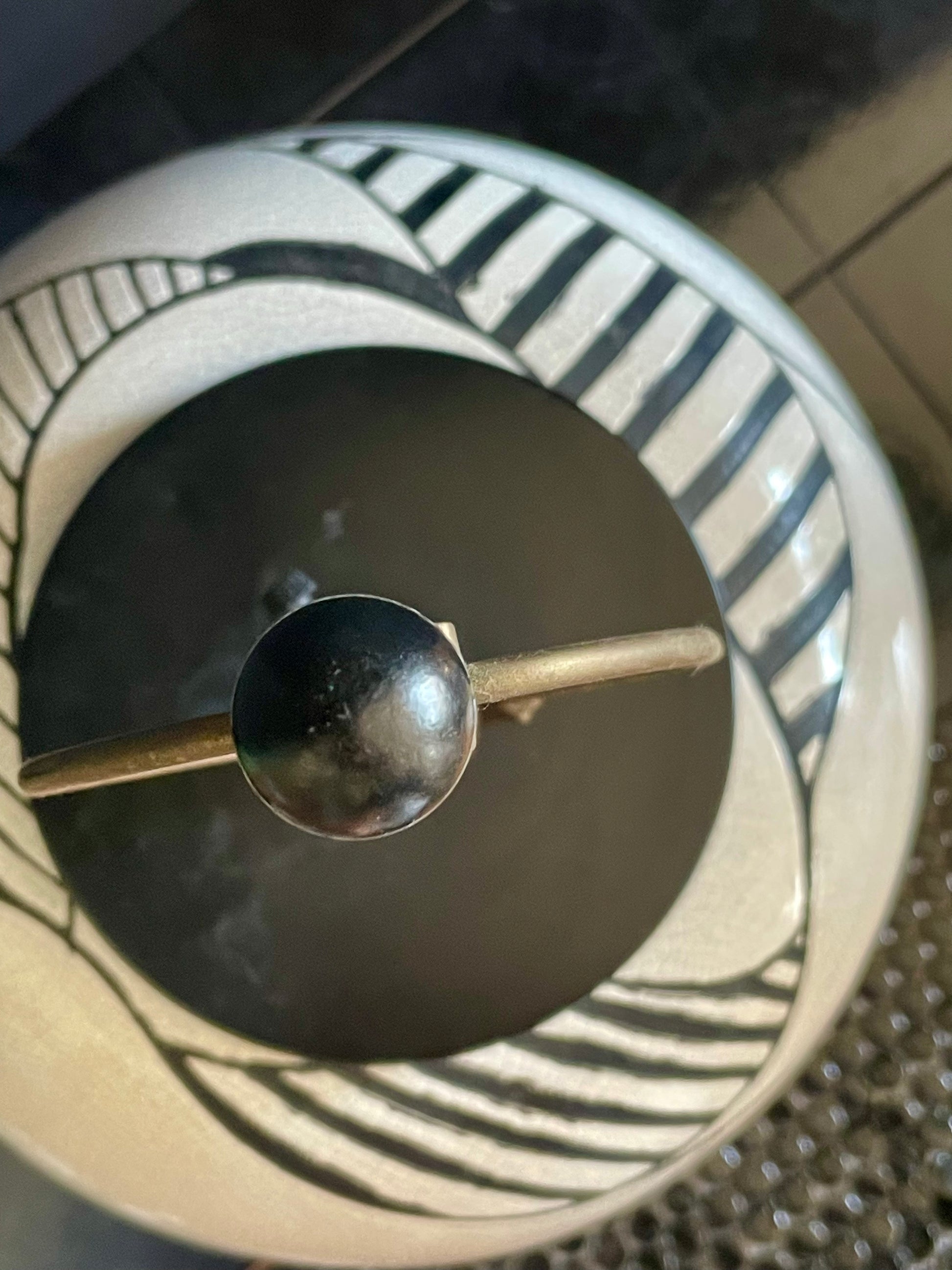 View from above of a round black and white ceramic table lamp showing the black ball finial in focus and the lamp and black tile background slightly out of focus.