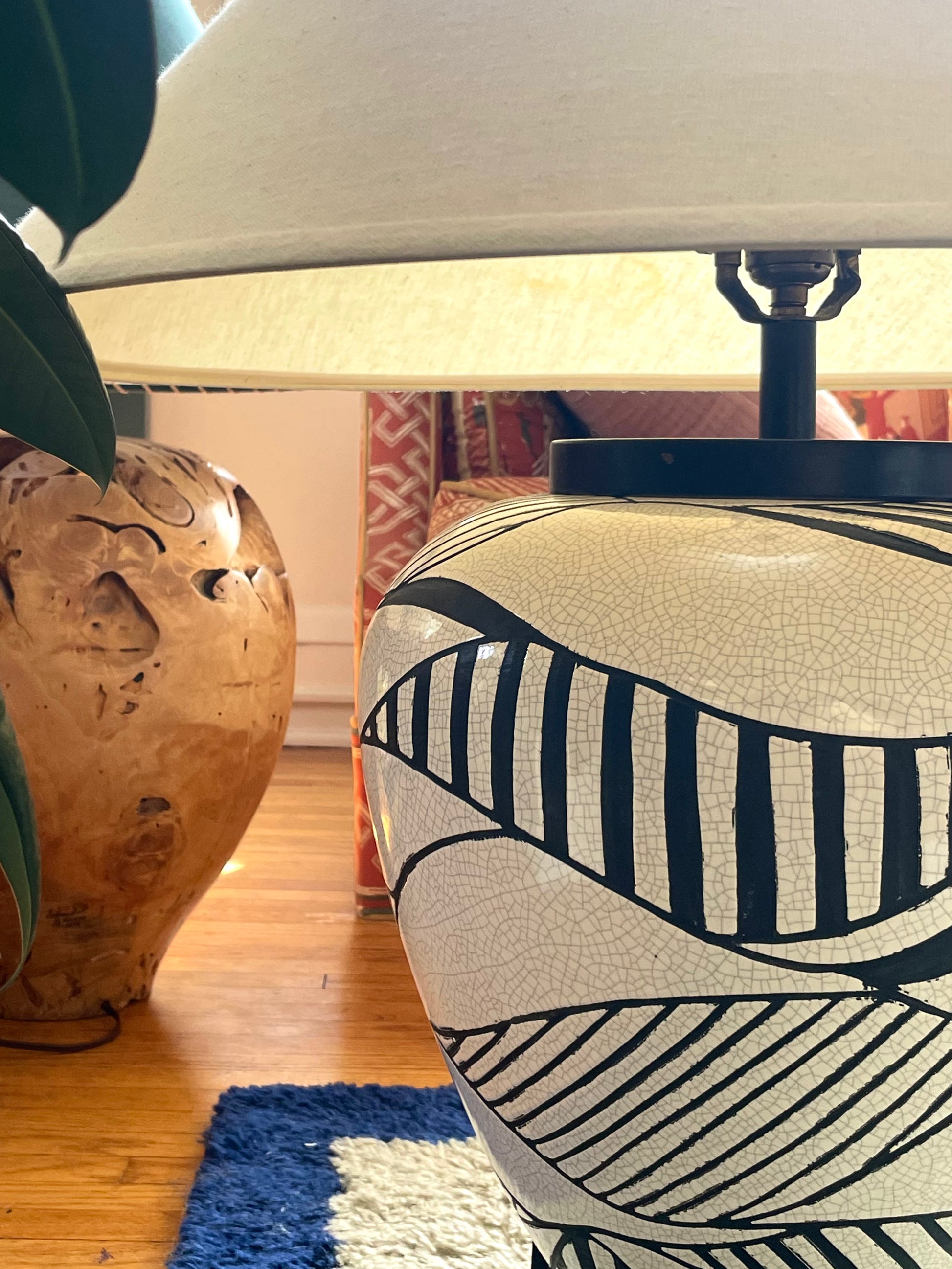 A ceramic table lamp with a black and white geometric-pattern base with white crackle glaze, shown next to a polished wood table lamp in a home interior setting.