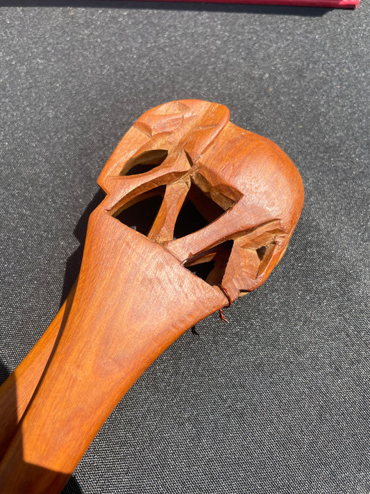Closeup of the top of a wood spoon, featuring a hand carved elephant, resting on a black surface.