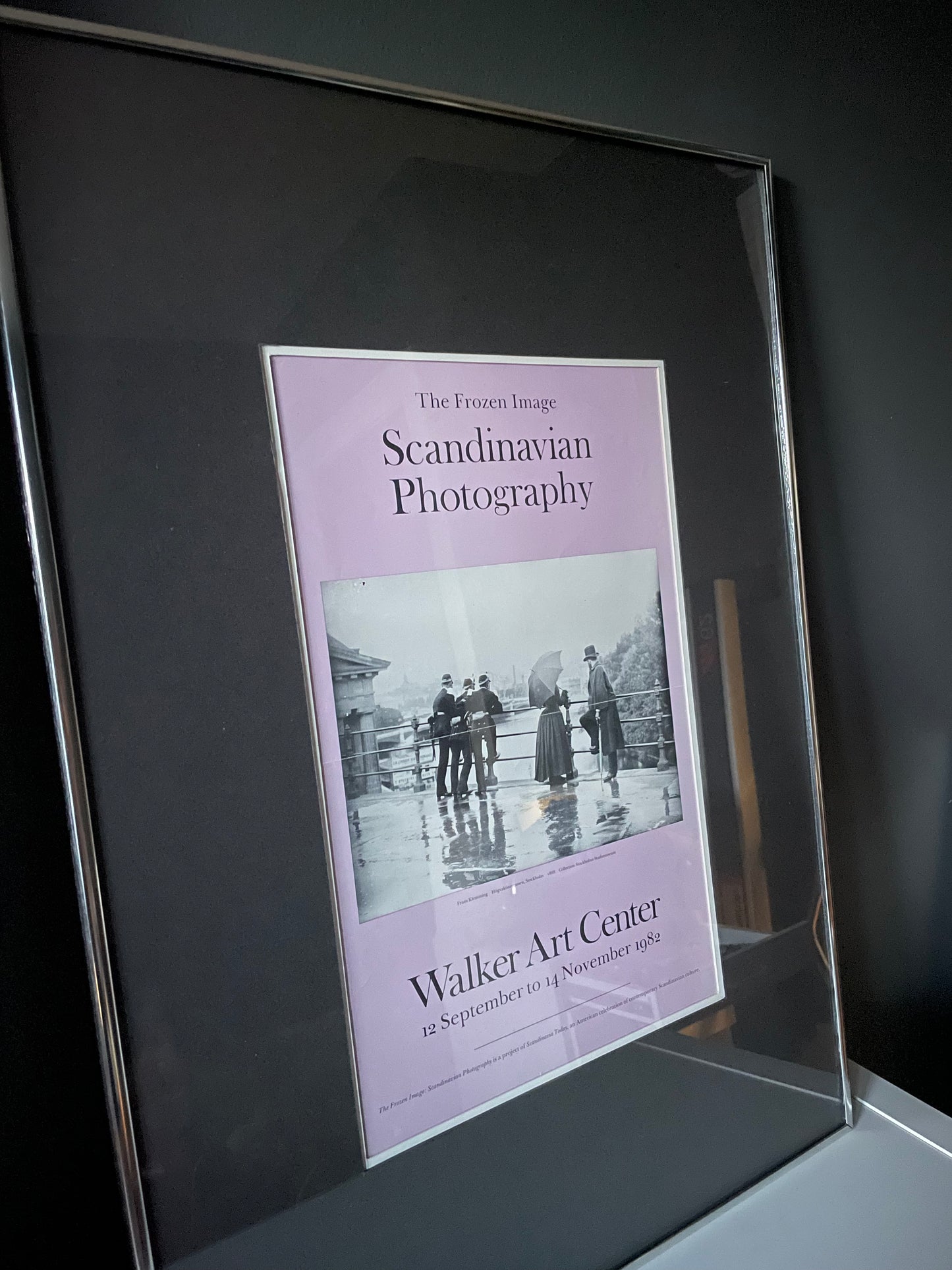 A framed lavender exhibition poster titled 'The Frozen Image: Scandinavian Photography’ for the Walker Art Center featuring a black-and-white historical photograph, shown in a silver gallery frame with grey matting.