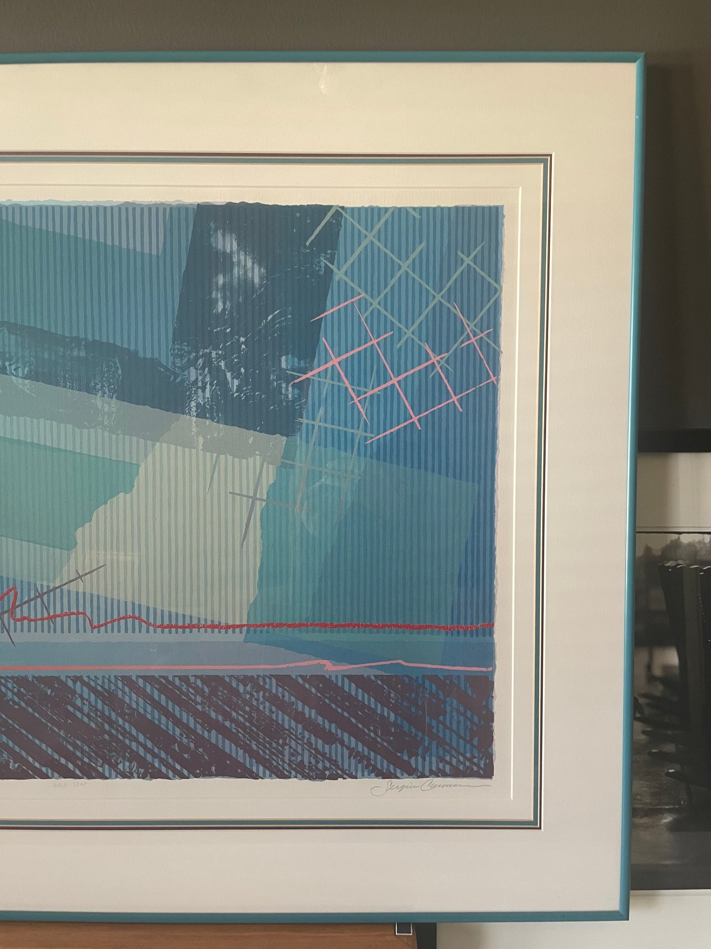A framed abstract art print featuring geometric shapes and textured brushstrokes in shades of blue, teal, white, and pink, with a wide white mat and a teal frame.