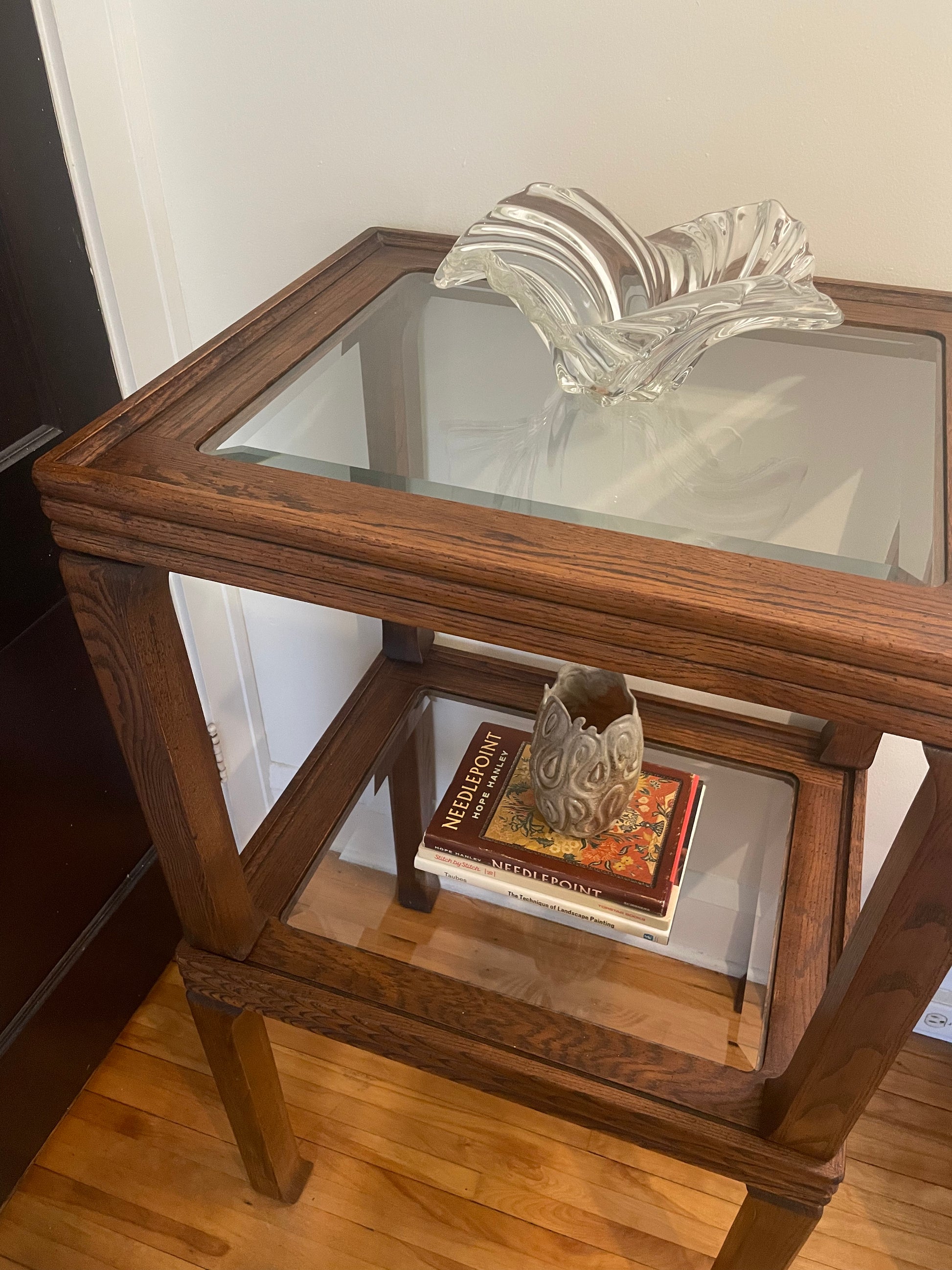Two glass-top rectangular wood side tables in a rich medium-dark broad shade stacked on top of each other and styled with a stack of books, ceramic vase, and glass bowl in a home setting.