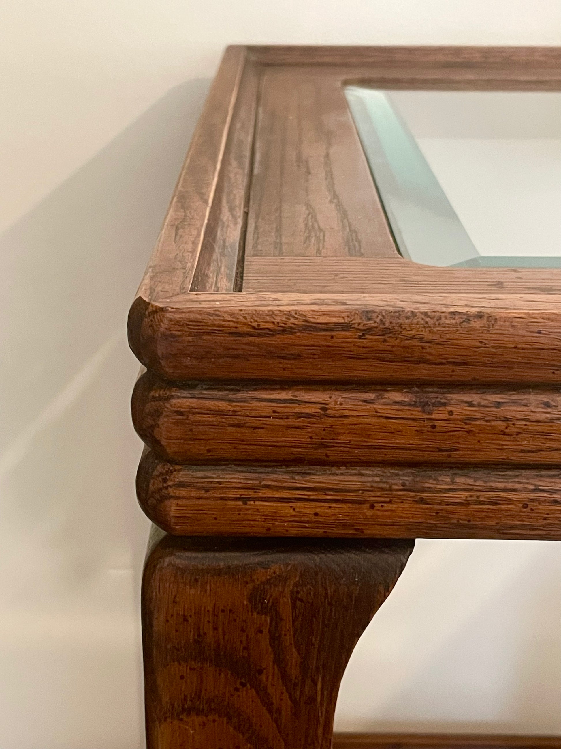 Close-up from the side of a carved wooden table corner with a glass top and rich medium-brown wood grain.
