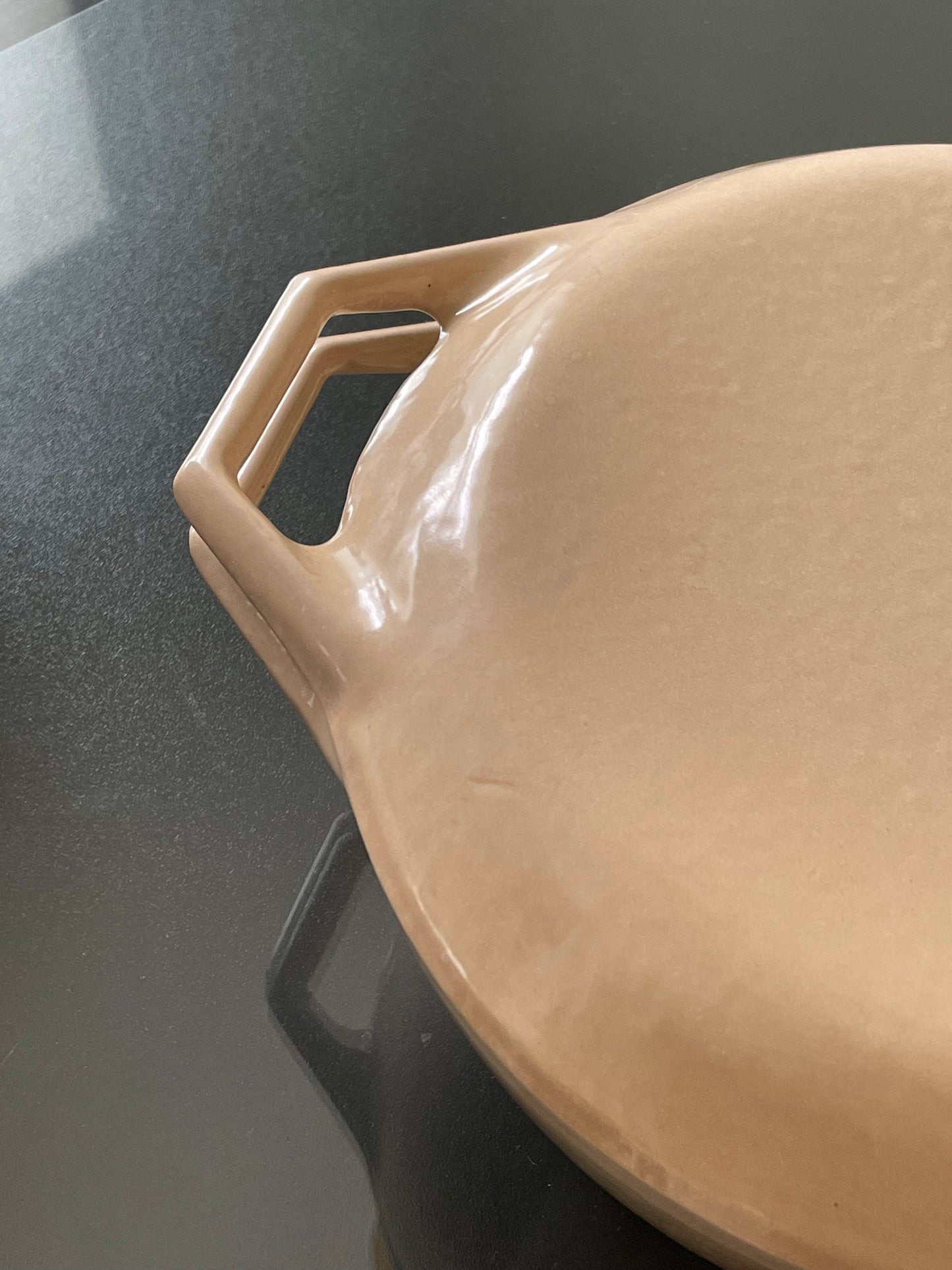 Close-up of a beige enameled dutch oven with an integrated handle, resting on a reflective black countertop.