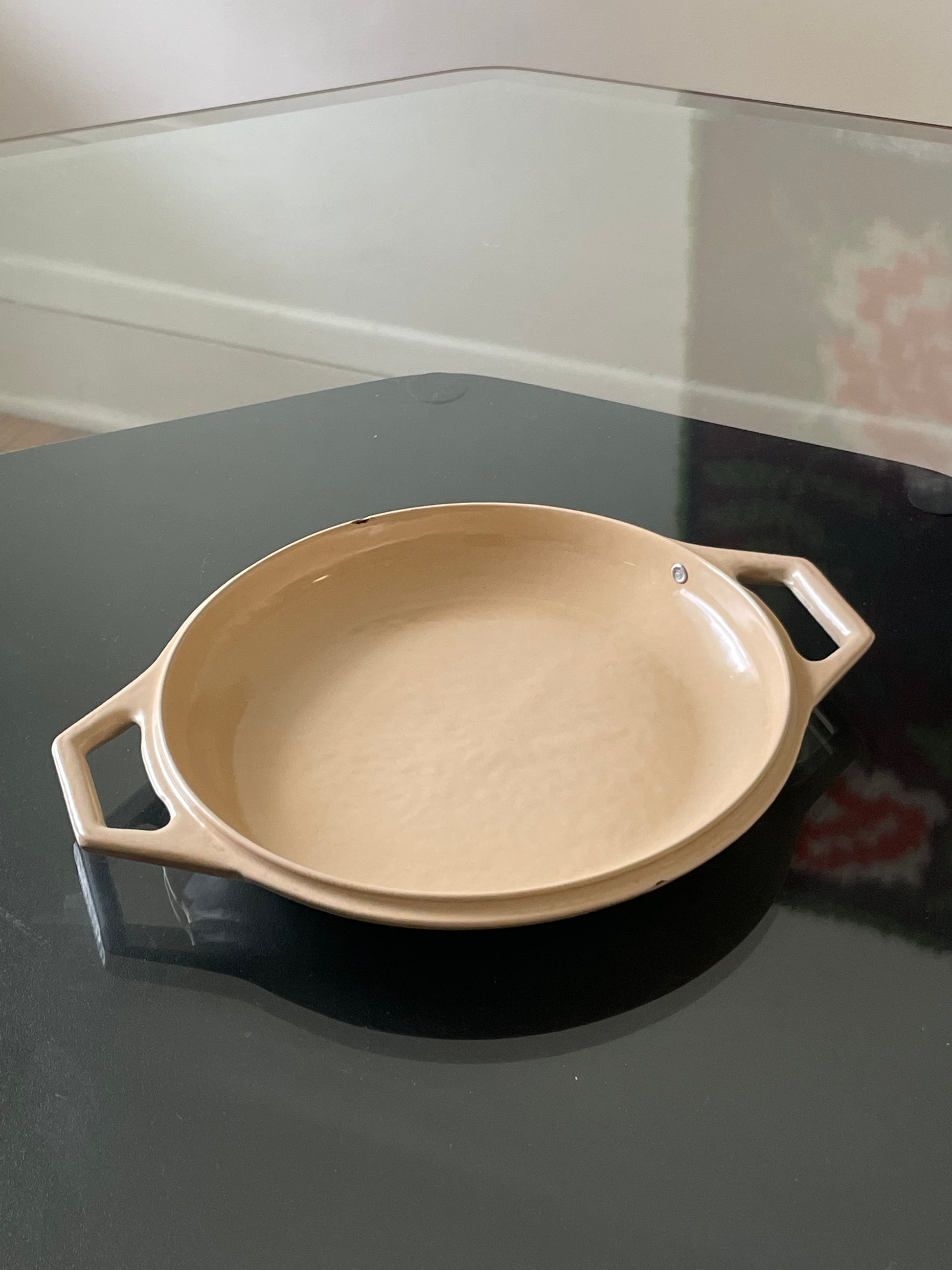 A beige enameled cast iron lid with side handles, resting on a dark reflective tabletop.