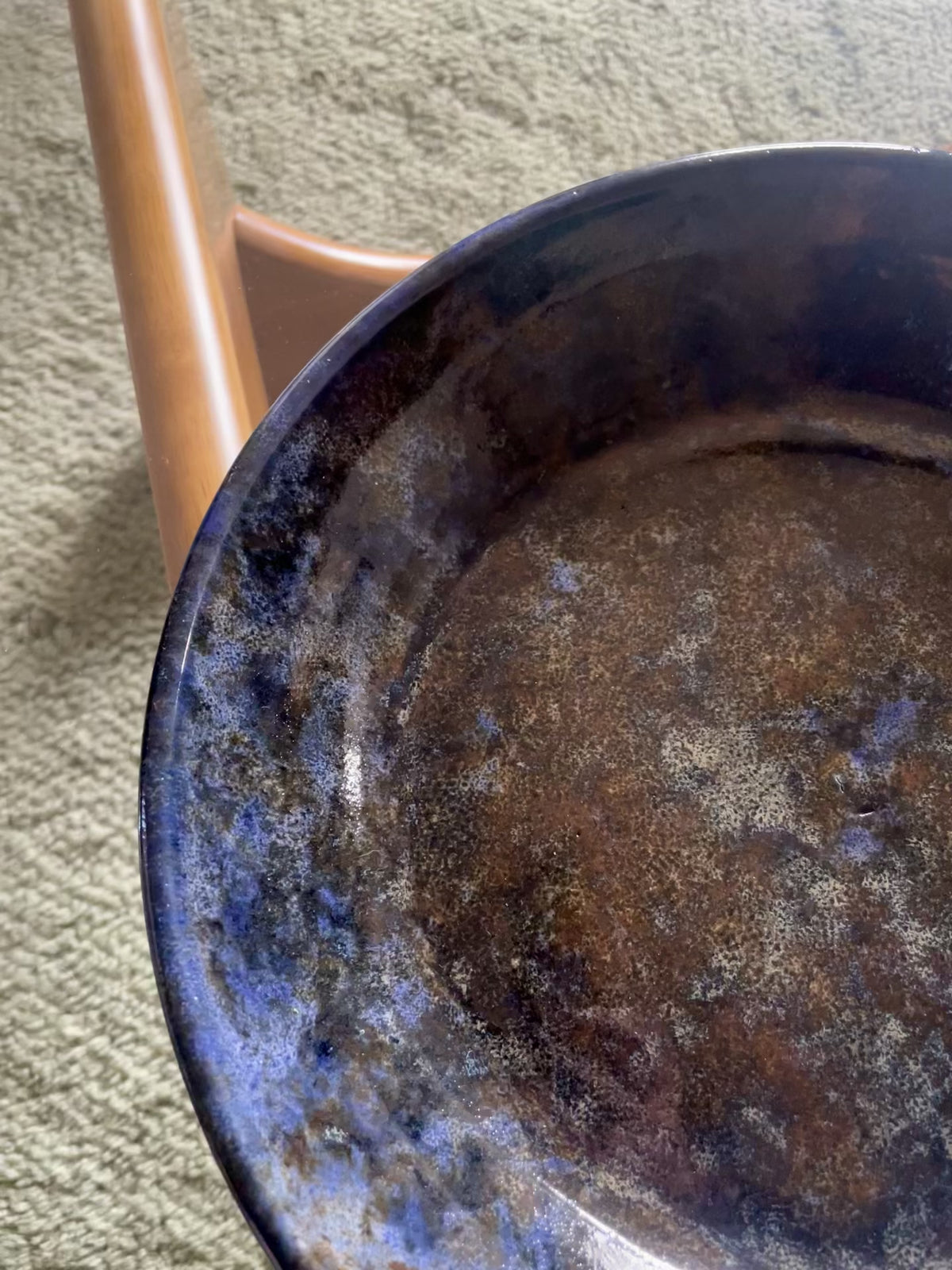 A video shows a close-up pan of a large round ceramic bowl with speckled blue and brown glazing rests on a glass table over a blue-grey rug.